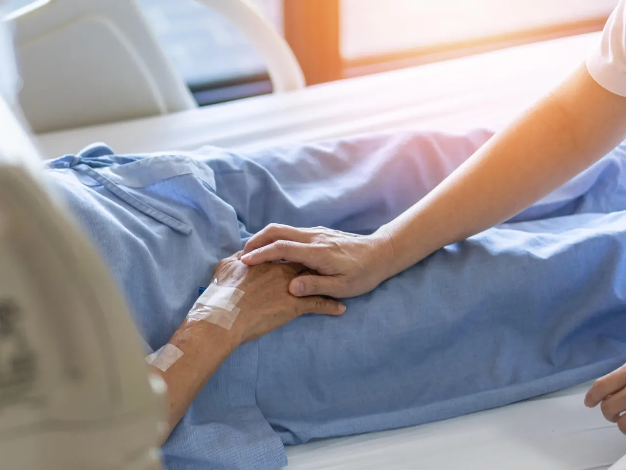 A caregiver holding the hand of a person in a hospital bed