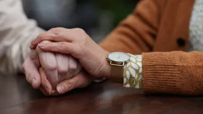 Caregiver holding hands with elderly person in supportive gesture